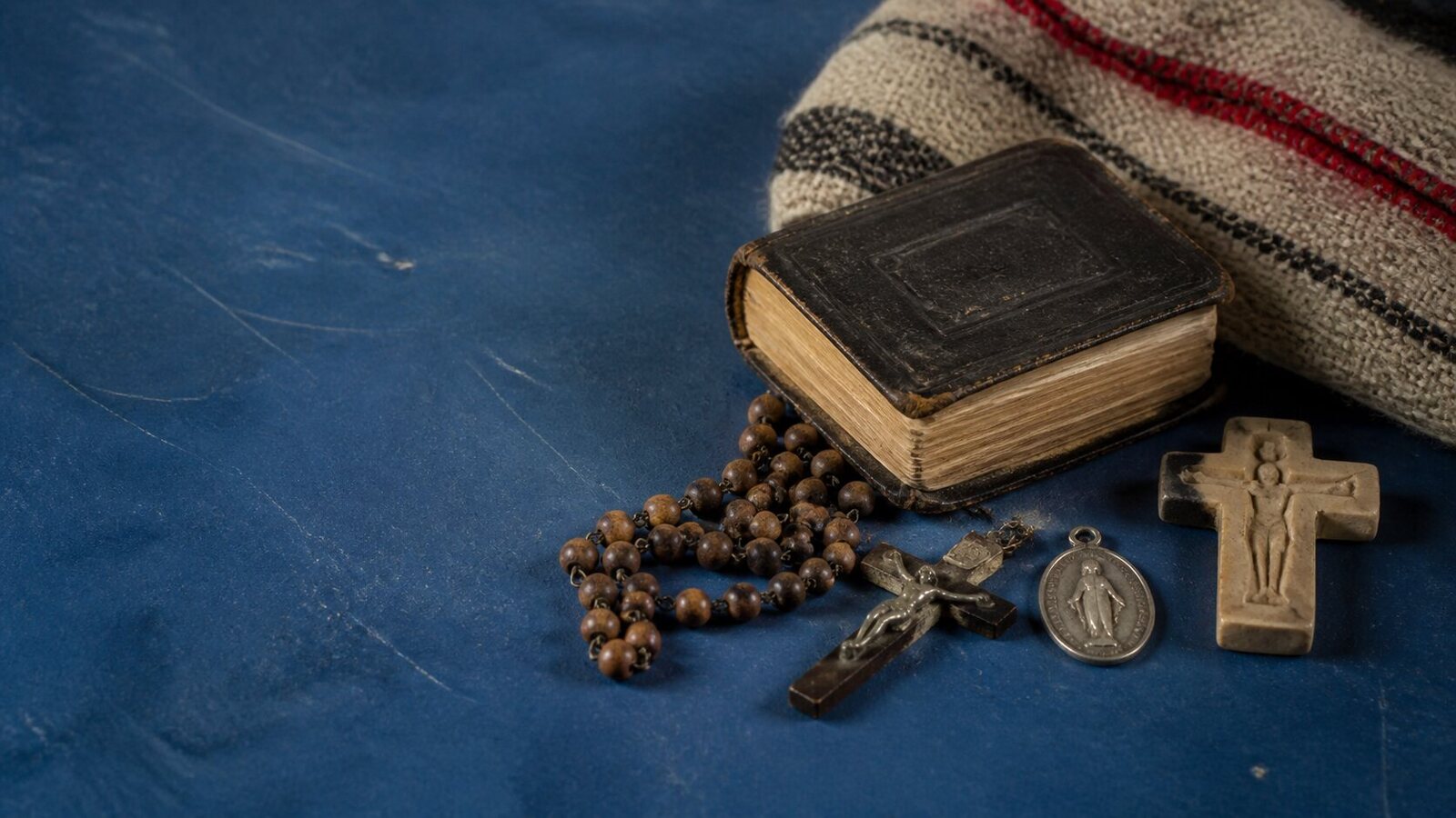 A rosary, missal, medal, textile, and small sacred image on a cobalt worktable